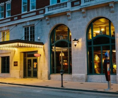 Historic hotel entrance with arched windows, outdoor lighting, and a warm, inviting atmosphere at dusk.
