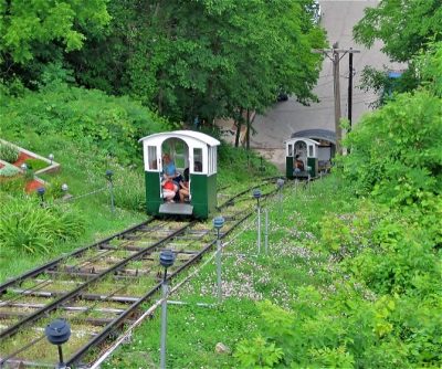 Funicular railway cars travel up a lush, green hillside, offering scenic views of the surrounding area.