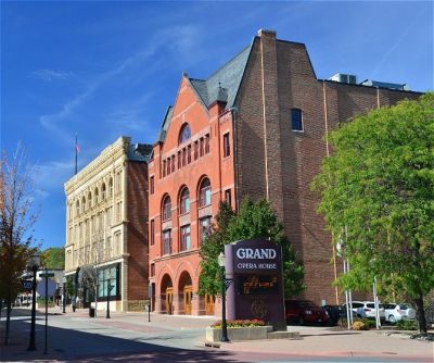 Historic red brick opera house with adjacent buildings, showcasing vibrant street views and greenery.