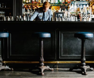 A bartender prepares drinks at a stylish hotel bar, featuring vintage stools and a well-stocked liquor display.