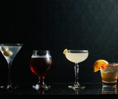 Four cocktails displayed against a dark background: martini, whiskey glass, sour cocktail, and an old-fashioned.