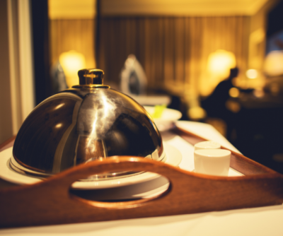 Silver cloche on a wooden tray with a small cup and plates, set in a luxurious hotel room with soft lighting.