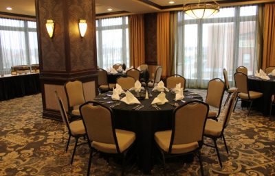Elegant hotel dining room with round tables set for guests, featuring napkins and large windows with natural light.