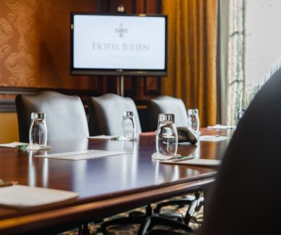 Well-appointed meeting room with brown and beige decor, featuring a large table, water bottles, and a presentation screen.