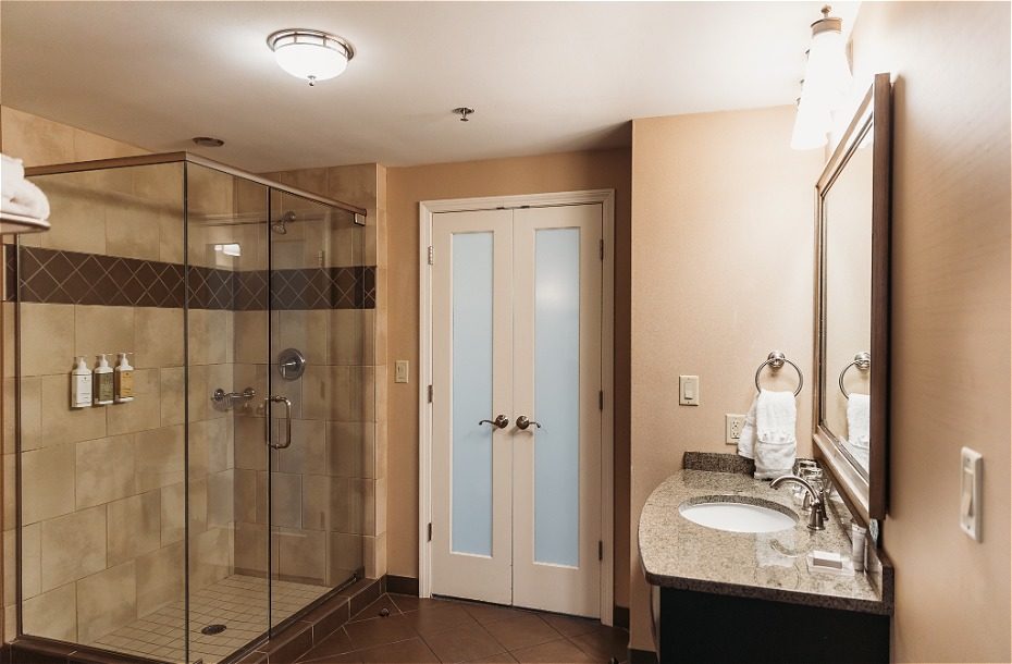 Spacious hotel bathroom featuring a glass shower, modern sink, and elegant lighting. Accessible double doors for privacy.
