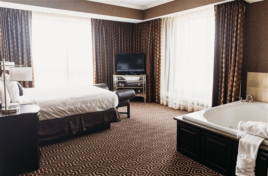 Spacious hotel room featuring a king bed, large windows, flat-screen TV, and a luxurious soaking tub.