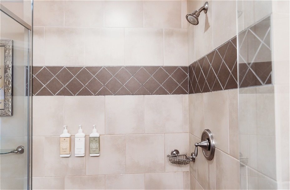 Modern hotel shower with tiled walls, adjustable showerhead, and shower amenities in sleek dispensers.