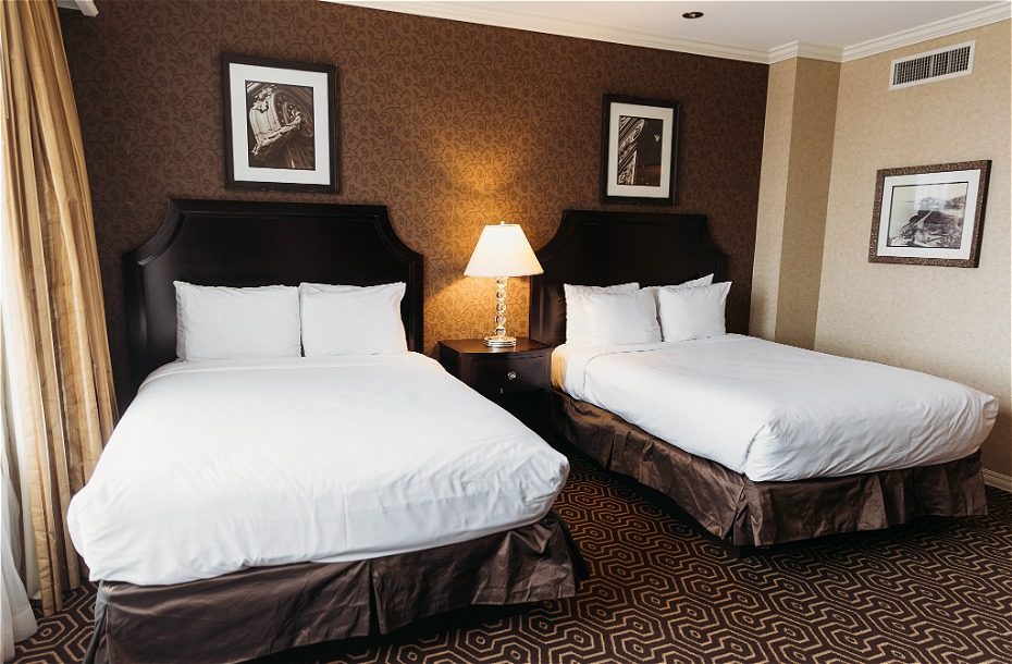 Modern hotel room with two queen beds, decorative wallpaper, bedside lamp, and framed art. Cozy and inviting atmosphere.