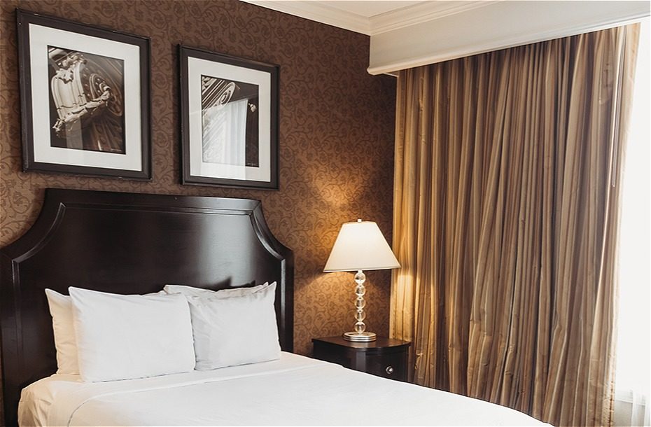 Cozy hotel room featuring a queen bed, elegant decor, two framed art pieces, and a bedside lamp with warm lighting.