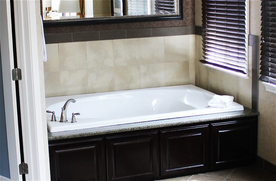 Spacious hotel bathroom featuring a large white soaking tub with a dark wood vanity and stylish tile accents.