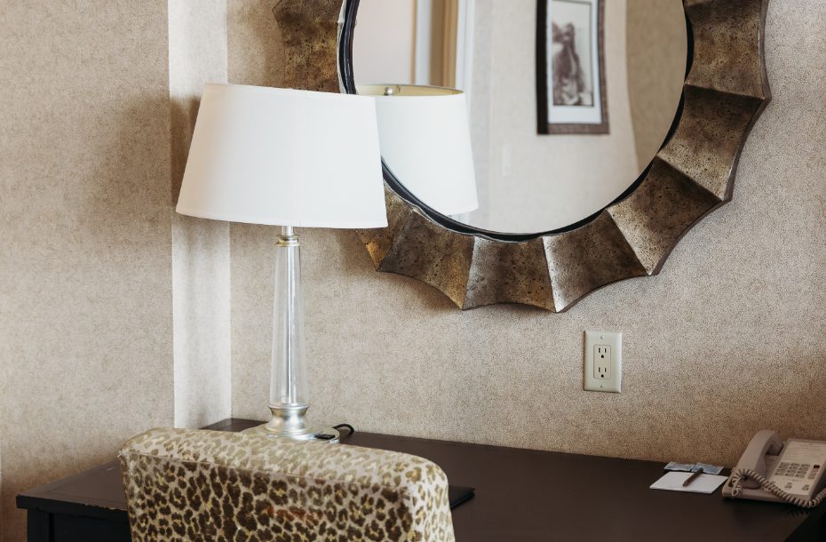 Stylish hotel desk with leopard-patterned chair, a sleek lamp, and a decorative round mirror above.