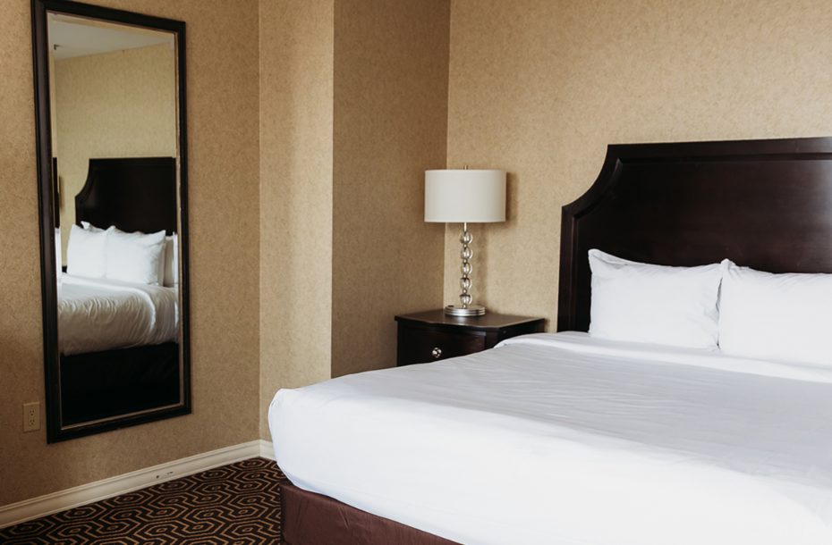 Cozy hotel room with a king-size bed, large mirror, bedside lamp, and warm-toned wallpaper.
