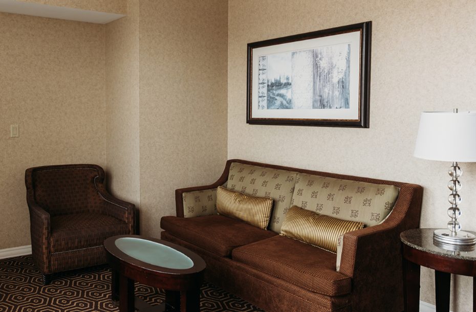 Cozy hotel seating area with a patterned sofa, armchair, coffee table, and decorative artwork on the wall.