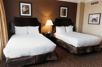 Double guest room with two beds, modern decor, warm lighting, and framed art on brown patterned walls.