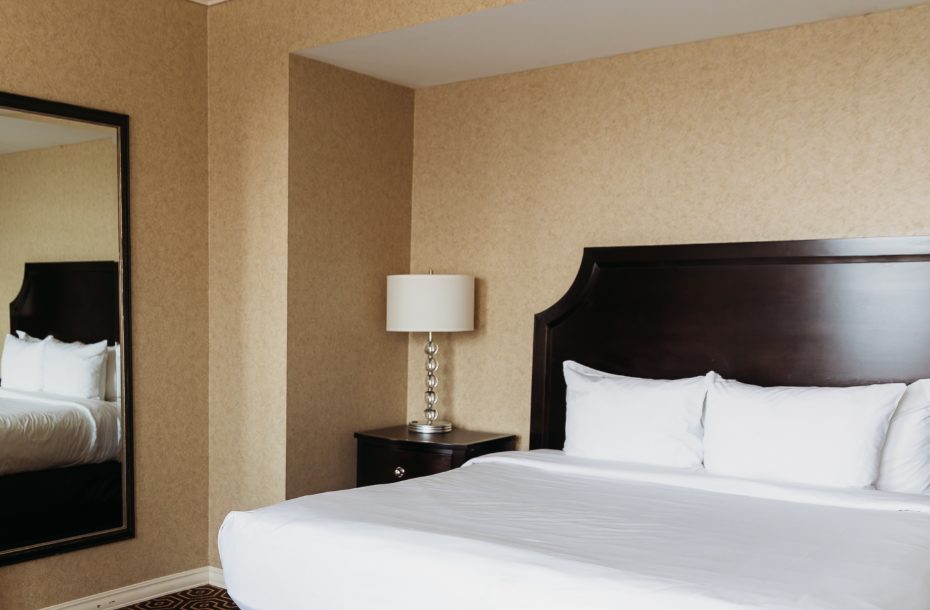Cozy hotel bedroom featuring a king-sized bed, bedside lamp, and a large mirror against a textured beige wall.