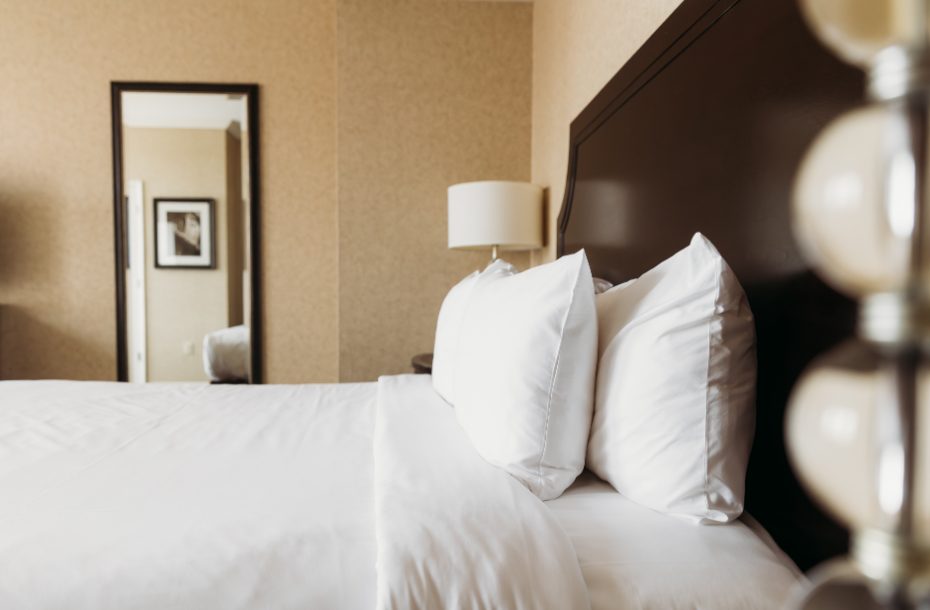 Cozy hotel room featuring a king-size bed with fluffy white pillows and a lamp, complemented by a stylish mirror.