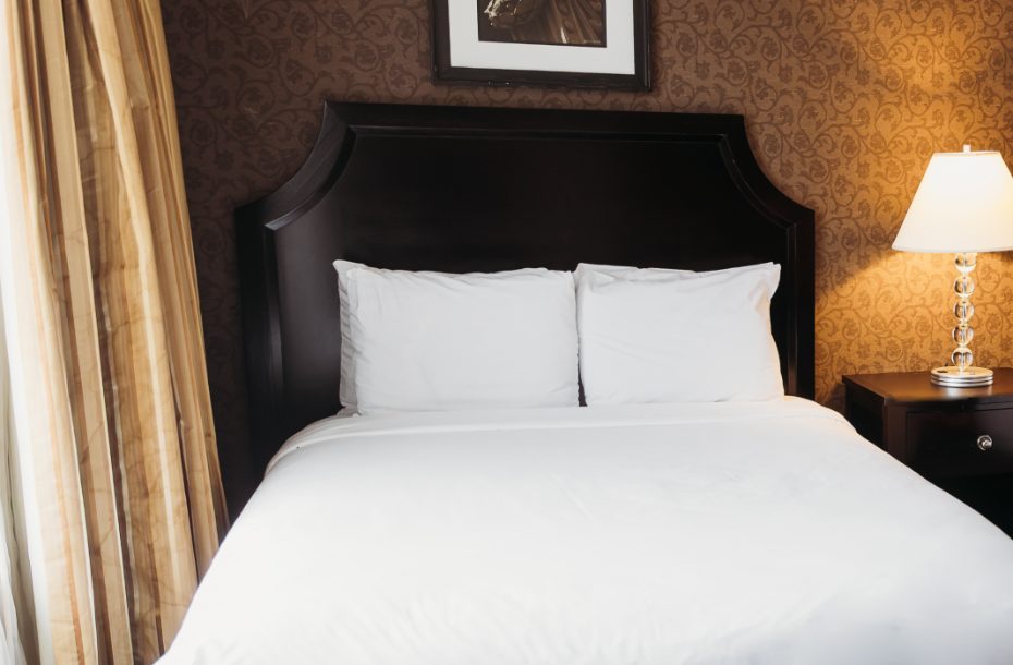 Cozy hotel room with a double bed, plush white linens, decorative wall, and a bedside lamp.