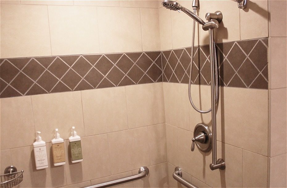 Modern hotel shower with a handheld showerhead, grab bars, and complimentary toiletries on the wall.
