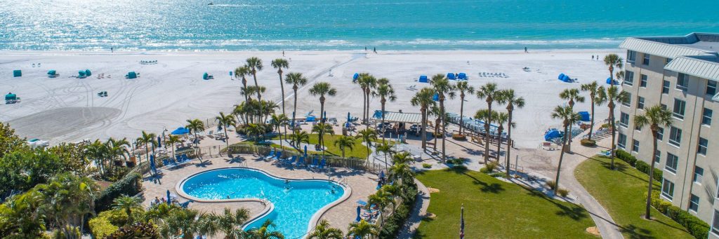 A beachfront hotel with a pool and palm trees.