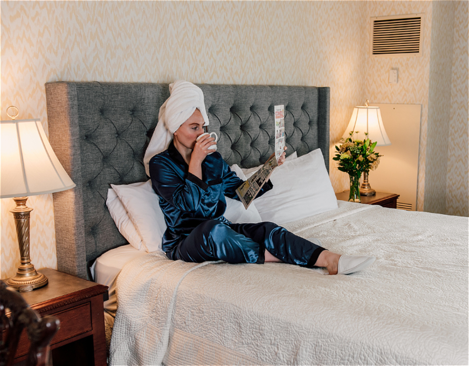 hotel guest sitting on bed reading newspaper and sipping coffee