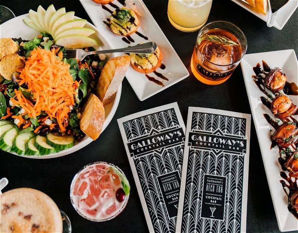 Various plates of food and cocktail drinks next to Galloways menus