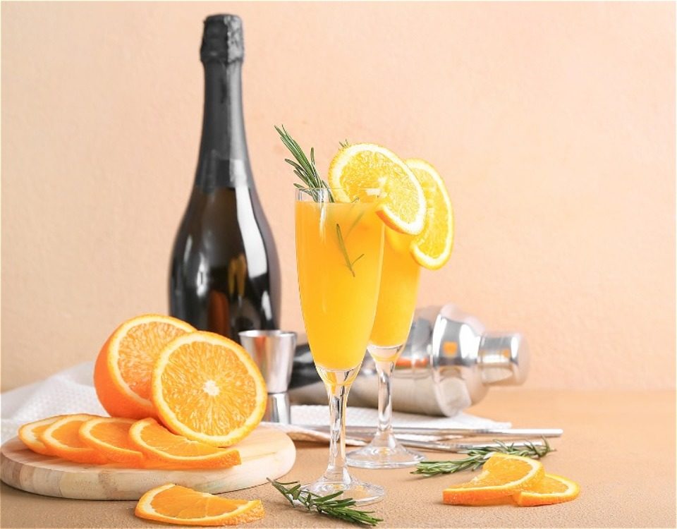 Bottle of champagne with two flutes of mimosas and orange slices