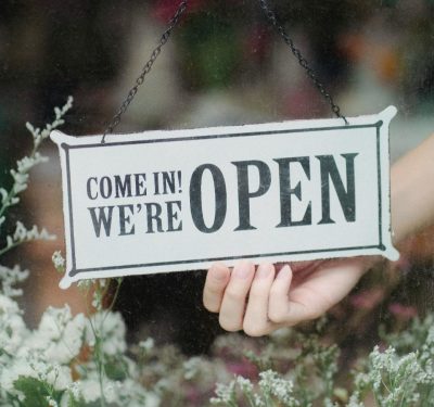 Hand holding a sign that says come in we are open