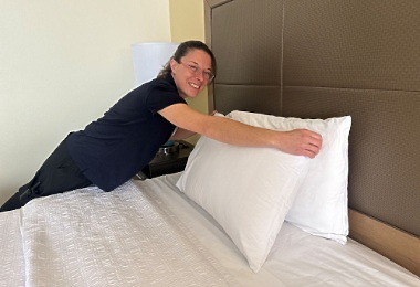 A young woman smiling while making a bed in a hotel room